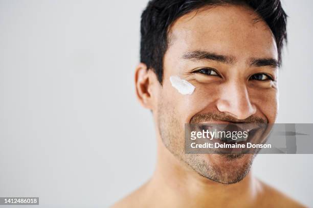 lotion or face cream on a confident and happy man's cheek with a bright smile. portrait of young attractive male with smooth skin and a good skincare routine with moisturizer under an eye - model smile stockfoto's en -beelden