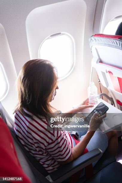 mature woman using mobile phone while sitting by the airplane window - thessaloniki airport stock pictures, royalty-free photos & images
