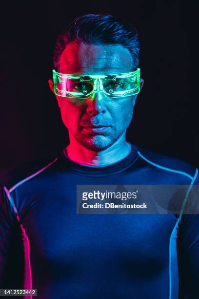 portrait of a man with cybernetic glasses with green lighting details and a tight blue t-shirt, in a blue and red environment, and a black background. robot, cyborg, future and metaverse concept. - asimo stock pictures, royalty-free photos & images