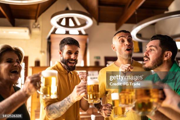 yellow and green sports fan celebrating and drinking beer at bar - saturday footy stock pictures, royalty-free photos & images