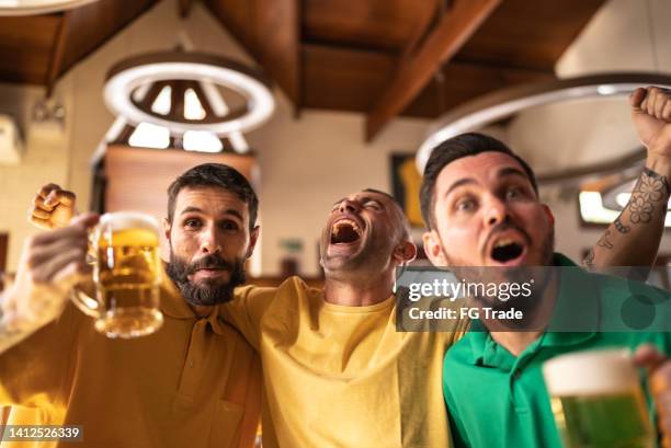 yellow and green sports fan celebrating and drinking beer at bar - saturday footy stock pictures, royalty-free photos & images