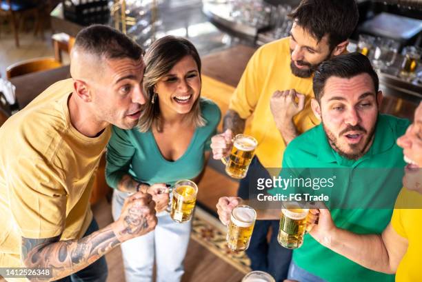 yellow and green sports fan celebrating and drinking beer at bar - australian pub stock pictures, royalty-free photos & images