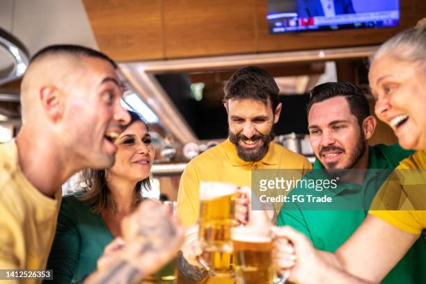 yellow and green sports fan celebrating and drinking beer at bar - saturday footy stock pictures, royalty-free photos & images