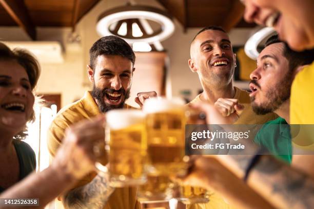 yellow and green sports fan celebrating and drinking beer at bar - saturday footy stock pictures, royalty-free photos & images