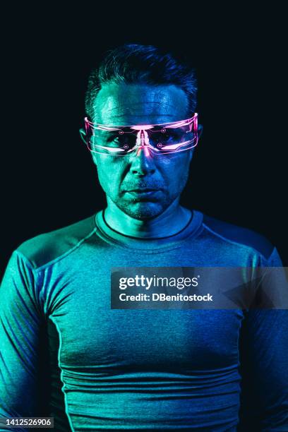 portrait of a man with cyber glasses with pink lighting details and a tight gray t-shirt, in a blue environment, and black background. robot, cyborg, future and metaverse concept. - asimo stock pictures, royalty-free photos & images