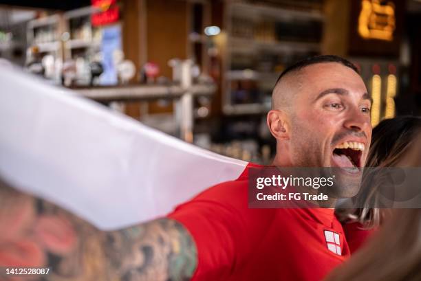 mid adult man celebrating english team winning in a bar - football fans celebrating stock pictures, royalty-free photos & images
