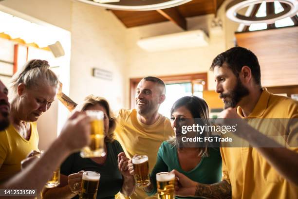 yellow and green sports fan celebrating and drinking beer at bar - saturday footy stock pictures, royalty-free photos & images