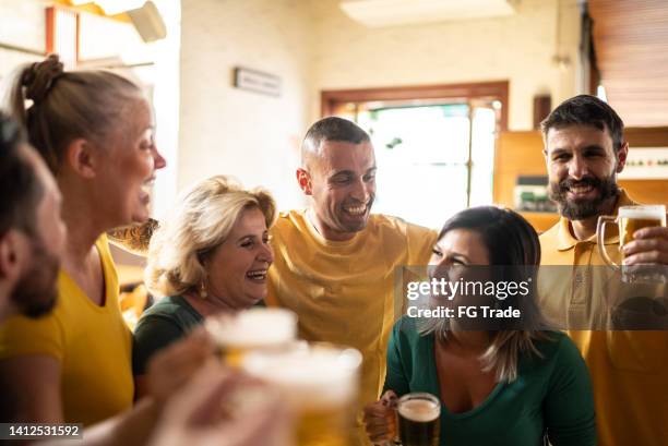 yellow and green sports fan celebrating and drinking beer at bar - saturday footy stock pictures, royalty-free photos & images