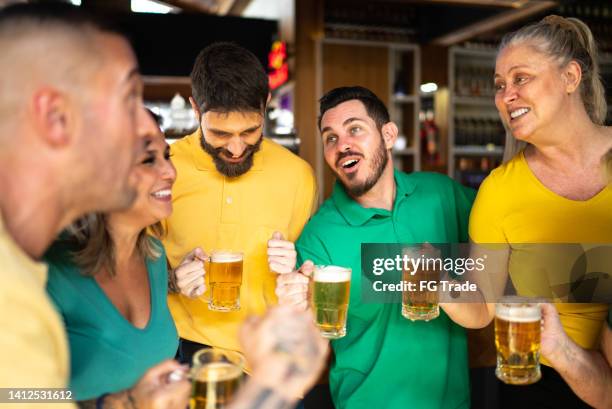 yellow and green sports fan celebrating and drinking beer at bar - saturday footy stock pictures, royalty-free photos & images