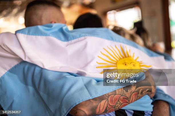 rear view of mid adult men embracing with argentinian flag in a bar - argentinian culture stockfoto's en -beelden