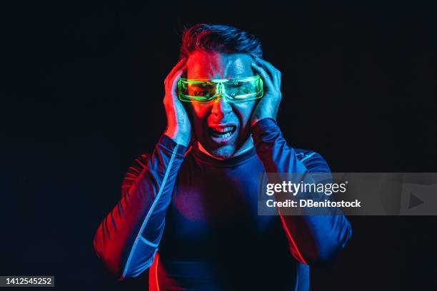 man with cybernetic glasses with green lights and a tight blue t-shirt, with his hands on his face, like crazy, in a blue and red environment, and a black background. robot, cyborg, future and metaverse concept. - asimo stock pictures, royalty-free photos & images