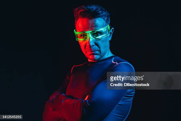 man with cybernetic glasses with green lights and a tight blue t-shirt, in profile, with his arms crossed, scared, in a blue and red environment, and a black background. robot, cyborg, future and metaverse concept. - asimo stock pictures, royalty-free photos & images