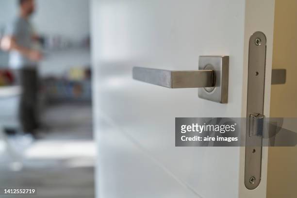 close-up of front view of modern metal entrance door handle to living room against standing unrecognizable man - doorknob stock pictures, royalty-free photos & images