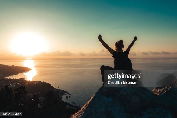 a person celebrating the dawn on the top of a cliff above the sea in the rays of the rising sun - hands sun stock-fotos und bilder