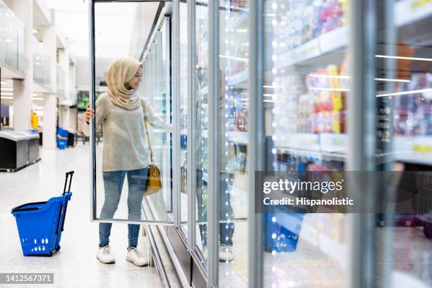 muslim woman buying groceries at the supermarket in the refrigerated section - dairy aisle stock pictures, royalty-free photos & images