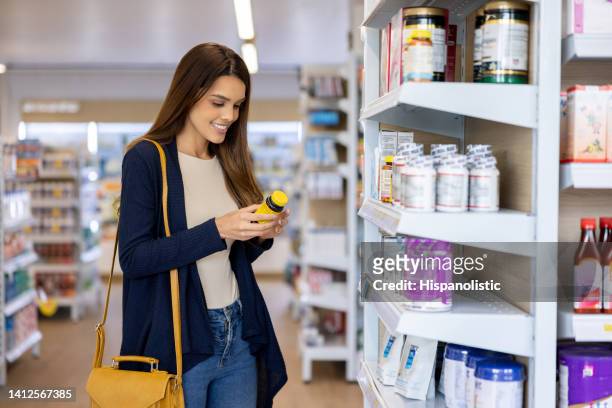 mujer comprando suplementos nutricionales en la farmacia - vitaminas fotografías e imágenes de stock