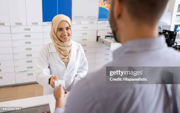 farmacéutico musulmán que vende algunos medicamentos a un cliente en la farmacia - atuendo religioso fotografías e imágenes de stock