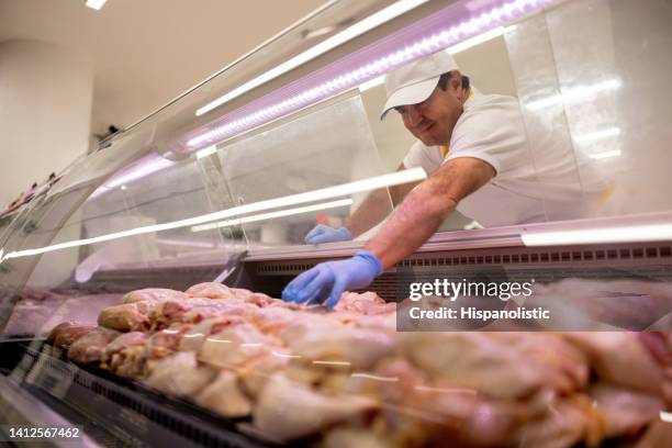 butcher working at a supermarket and grabbing a piece of chicken - slaktare bildbanksfoton och bilder