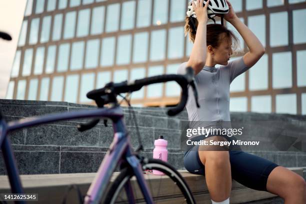 young cyclist woman take off helmet on head - protective sportswear stock-fotos und bilder