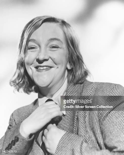 Beryl Reid , British actress, smiling as she adjusts her tie in a studio portrait, against a white background, circa 1965.