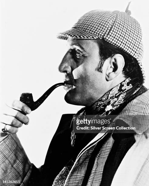 Basil Rathbone , British actor, wearing a deerstalker hat and smoking a pipe, in profile, in a studio portrait, against a white background, circa...