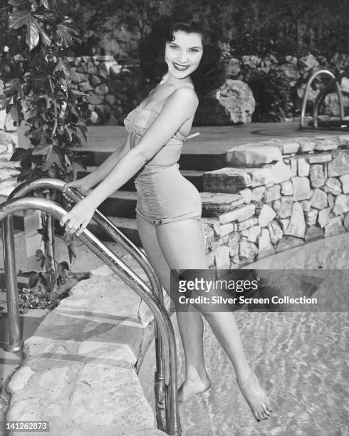 Full length portrait of Debra Paget, US actress, wearing a swimsuit, smiling as she stands on a pool ladder, at the edge of a swimming pool, circa...