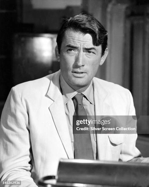 Gregory Peck , US actor, wearing a white jacket over a white shirt, with a dark tie, in a studio portrait, against a dark background, circa 1965.