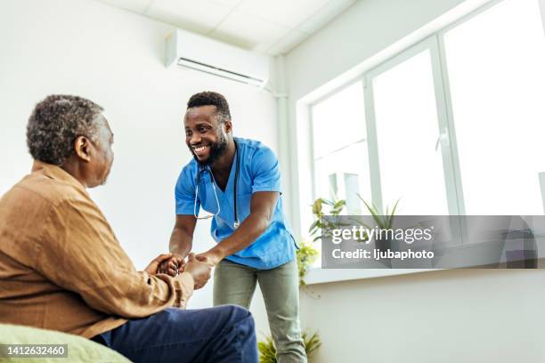 männliche krankenschwester, die die hände eines älteren mannes bequem hält. - nurse with old male patient home care stock-fotos und bilder