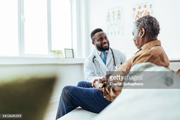 male family doctor listening carefully to a senior man patient problems and symptoms - doctor and patient talking imagens e fotografias de stock