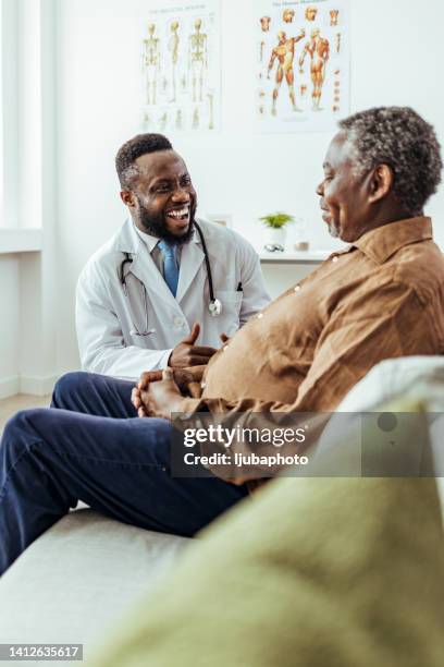 doctor smiles and tries to encourage sad senior man - african doctor stock pictures, royalty-free photos & images