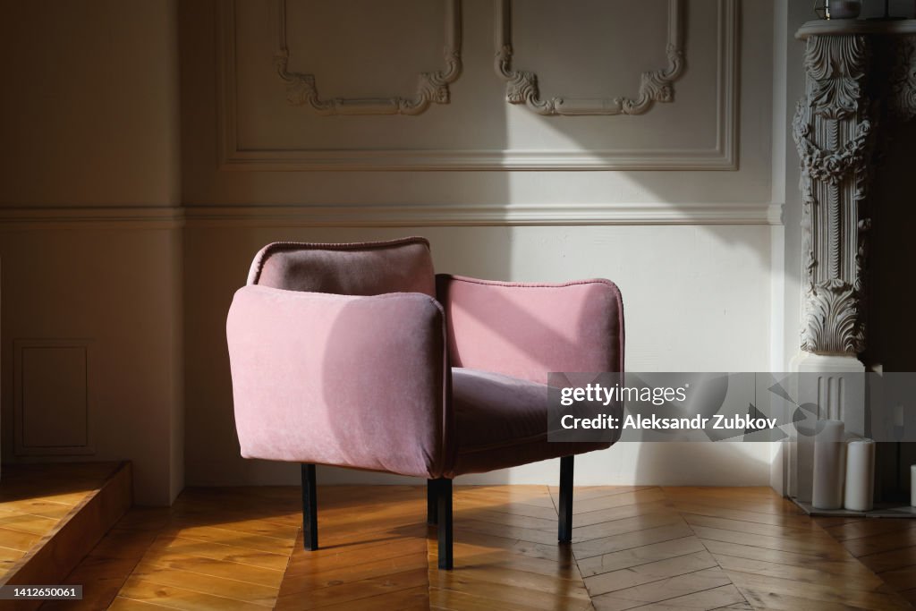 The interior of the living room is made in English style with a pink velour armchair against a light wall, with a wooden floor or parquet. Home improvement. Beautiful luxurious modern interior.