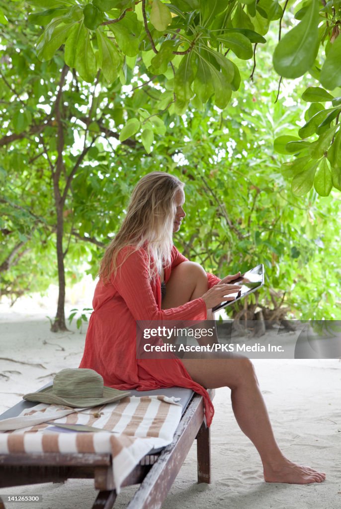 Woman uses digital tablet from bench in jungle