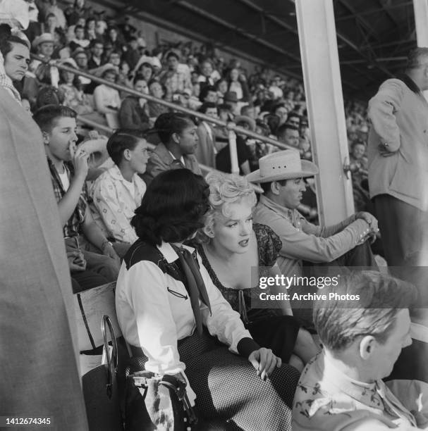 American actress Eileen Heckart and American actress Marilyn Monroe sitting with people in the rodeo scene from the film 'Bus Stop, ' filmed at the...