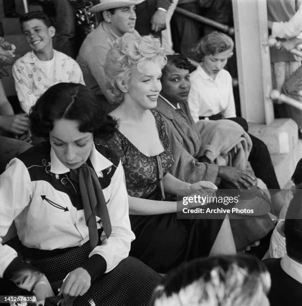 American actress Eileen Heckart and American actress Marilyn Monroe sitting with people in the rodeo scene from the film 'Bus Stop, ' filmed at the...