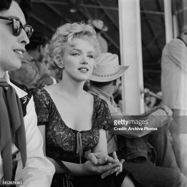 American actress Eileen Heckart and American actress Marilyn Monroe sitting with people in the rodeo scene from the film 'Bus Stop, ' filmed at the...