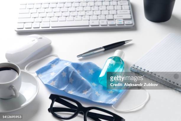 safety and hygiene measures in the office. preventing the spread of the covid-19 virus. protective reusable stitched face mask, keyboard, computer mouse, pen with notepad, black coffee mug, hand sanitizer, glasses, on the desktop, white background. - siberian mouse fotografías e imágenes de stock