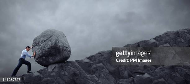 man rolling rock up hill - inspanning stockfoto's en -beelden