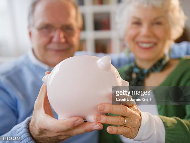 senior couple holding piggy bank - couple saving piggy bank stock pictures, royalty-free photos & images