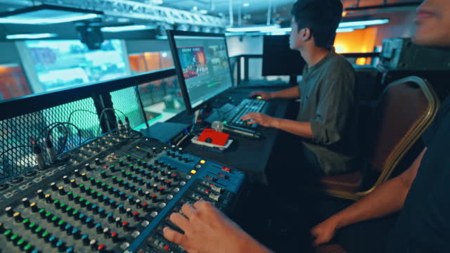 무대 조명, 사운드 시스템 및 조명 효과에 대한 제어판이있는 무대 뒤에서 일하는 아시아 스포츠 이벤트 승무원