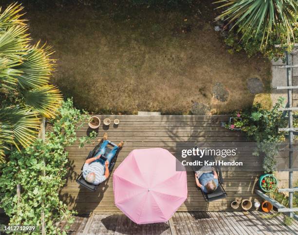 a couple relaxing in a suburban garden summer - sonnenschirm stock-fotos und bilder