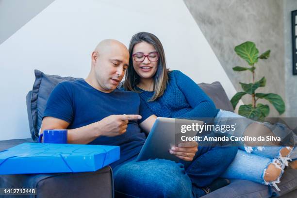 brazilian couple sitting on the sofa, using an ipad - amanda blue stock pictures, royalty-free photos & images