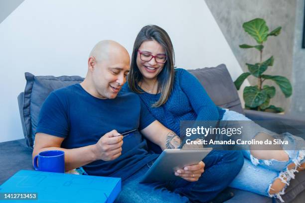 brazilian couple sitting on the sofa, using an ipad - amanda blue stock pictures, royalty-free photos & images