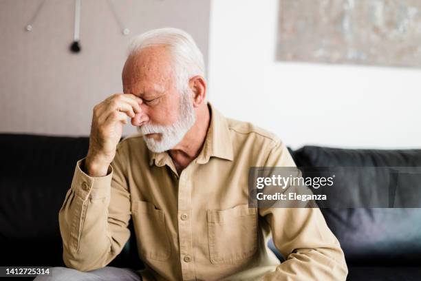 shot of a handsome senior man suffering with a headache at home - handsome people photos stock pictures, royalty-free photos & images