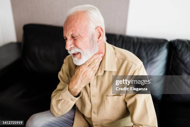 älterer mann, der seine entzündeten mandeln reibt, mandelentzündungsproblem. mann mit schilddrüsenproblemen, berührt seinen hals, mann hat halsschmerzen - kehle stock-fotos und bilder