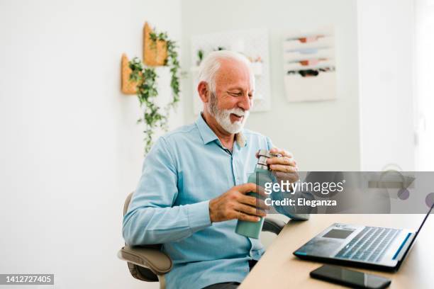 senior man drinking water from reusable bottle at office - reusable water bottle office stock pictures, royalty-free photos & images
