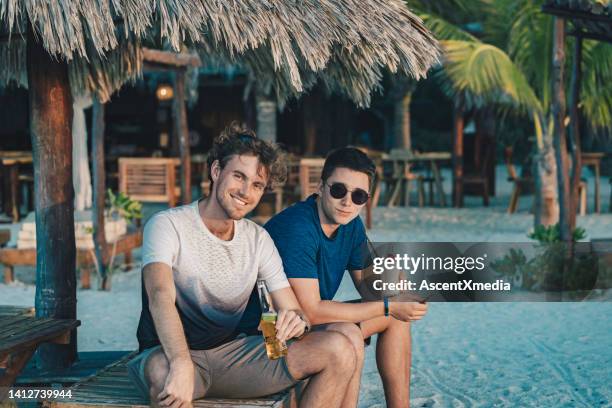 two young men relax by the pool with drinks - blue shorts stock pictures, royalty-free photos & images