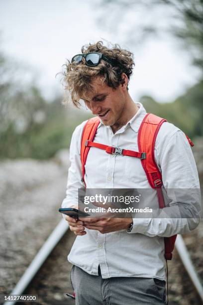 young man uses mobile phone on train tracks - red shirt stock pictures, royalty-free photos & images