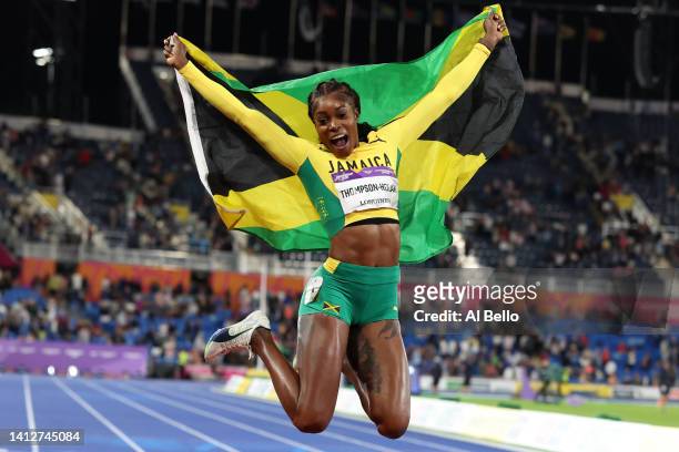 Elaine Thompson-Herah of Team Jamaica celebrates with their countries flag after winning the gold medal in the Women's 100m Final on day six of the...