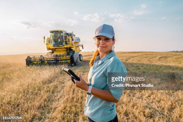 una agricultora sostiene una tableta digital en un campo agrícola. agricultura inteligente - agricoltura fotografías e imágenes de stock