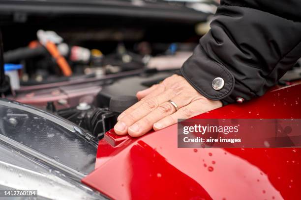 close-up of side of hand of a woman leaning on her red car under the hood of the car while waiting for service during a clear day - car engine close up stock pictures, royalty-free photos & images